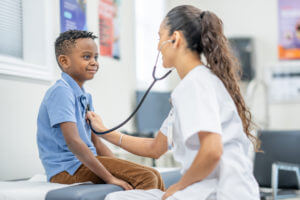 A young boy sits up on an exam table in a pediatrician office during a routine check-up