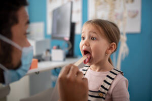 pediatrician checking little girl's throat in his offic